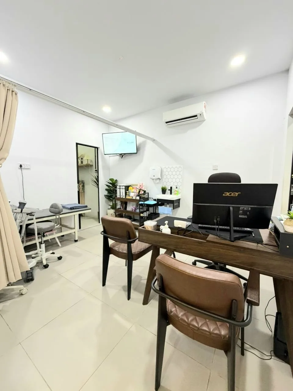 Bilik konsultasi am di Klinik Hazcare — meja kayu, kerusi kulit, monitor di belakang.