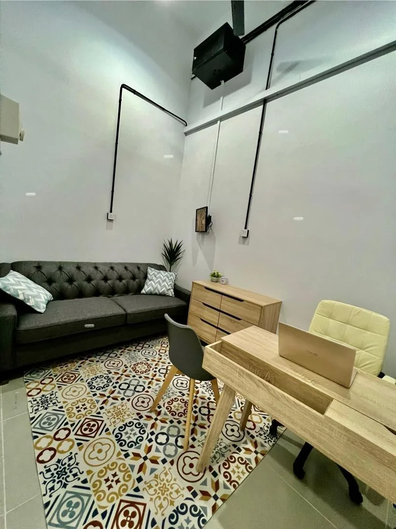 Bilik kaunseling Klinik Minda Hazcare — sofa chesterfield kelabu, meja kayu, lantai dengan corak hangat, lampu lembut.